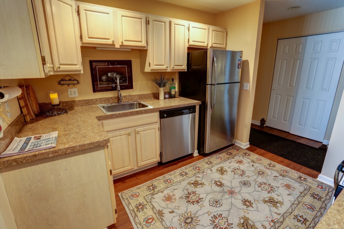 A cozy kitchen with wooden cabinets, stainless steel appliances, and a decorative rug.