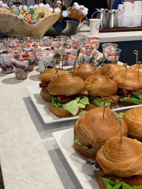 A platter of sandwiches arranged on a buffet table with various appetizers in the background.