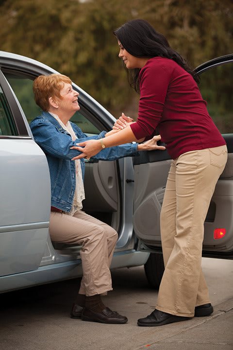 A person assisting an elderly woman out of a car.