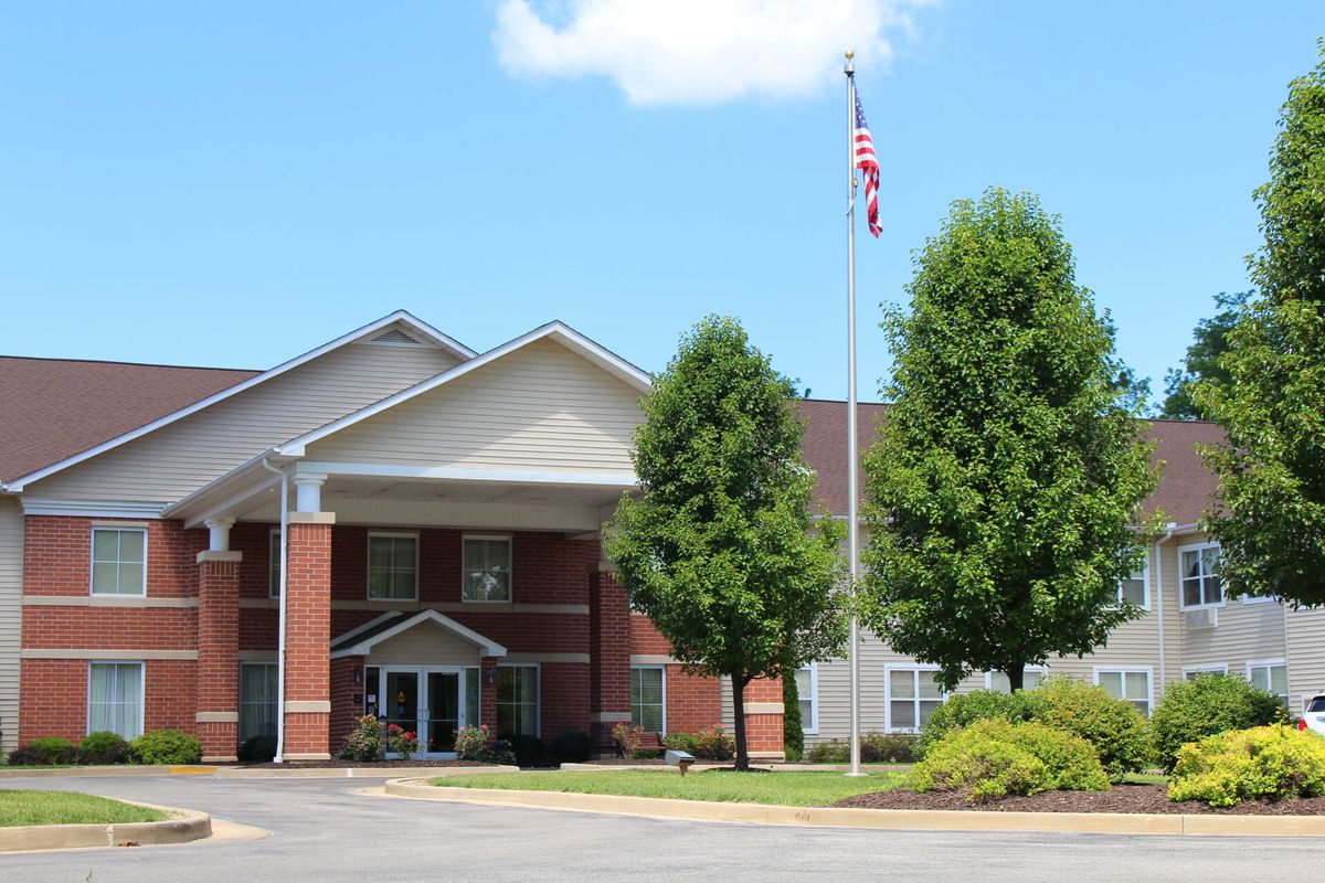 A mid-sized building with a brick facade and a flagpole in front, surrounded by trees under a clear sky.