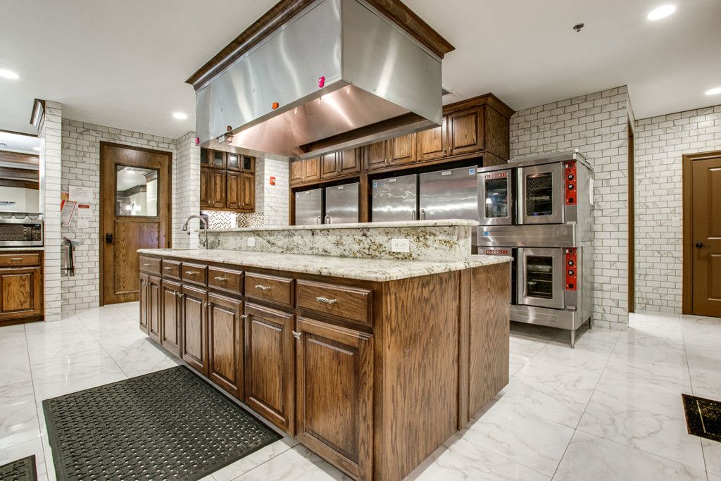 A modern kitchen with wooden cabinetry, a central island featuring a granite countertop, and industrial stainless steel appliances.
