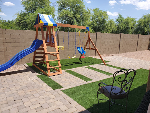 A colorful wooden playground set featuring a slide and swings, nestled in a well-maintained backyard with artificial grass.