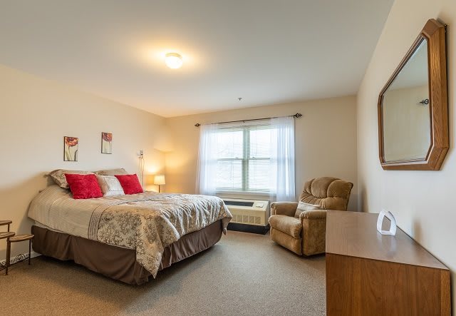 A cozy bedroom interior with a comfortable bed and an armchair next to the window.