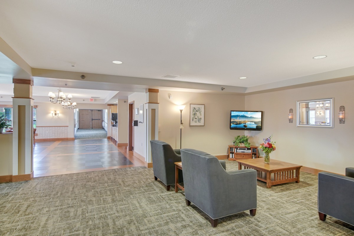 A well-lit lobby area featuring comfortable seating, a television, and a hallway leading to other rooms.