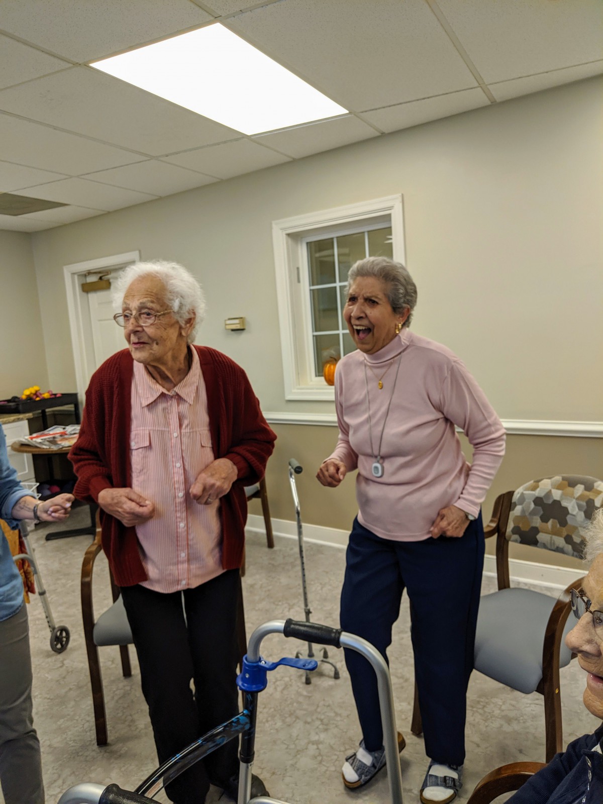 Two elderly women enjoying a moment together indoors, using walking aids.