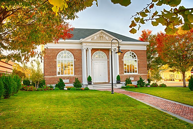 A beautiful brick building with classic columns and a well-maintained green lawn, surrounded by autumn trees.