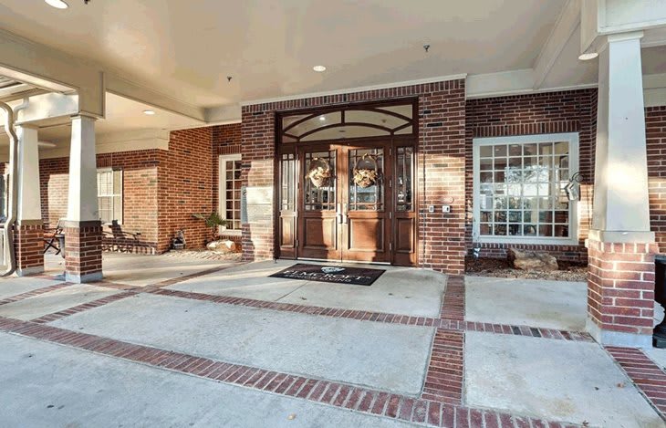 A welcoming entrance with double doors adorned with wreaths, set in a brick facade and framed by large windows under a covered porch.
