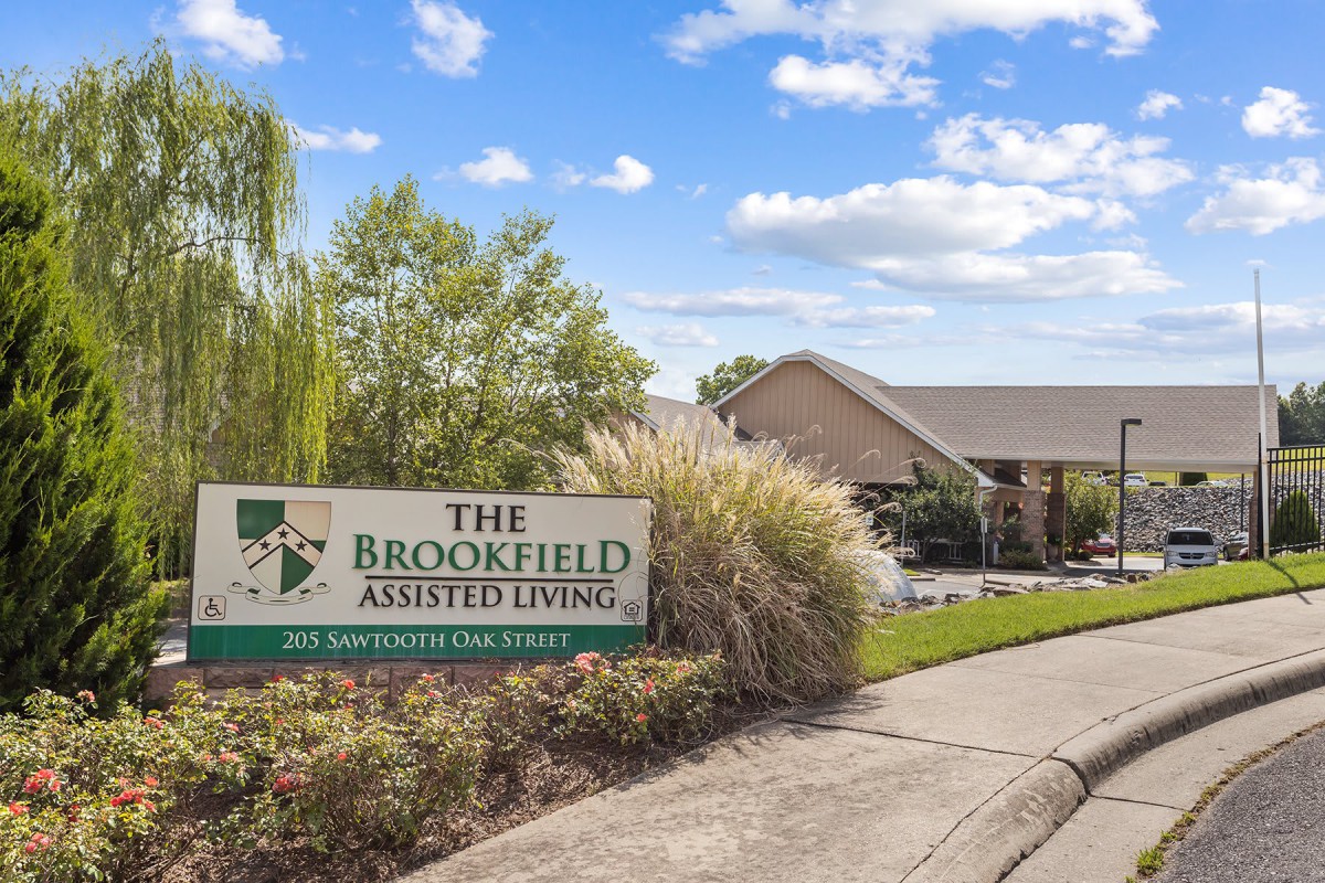 The entrance to The Brookfield Assisted Living, featuring a well-maintained landscape and a welcoming sign.