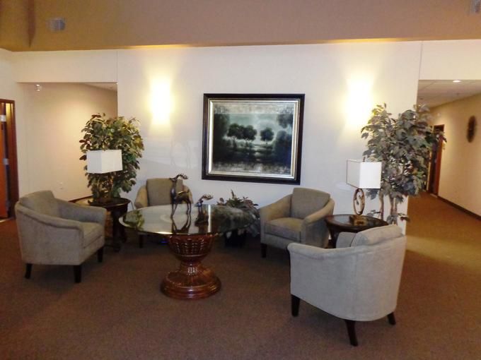 A cozy waiting room featuring a seating area with chairs, a coffee table, decorative plants, and artwork on the wall.