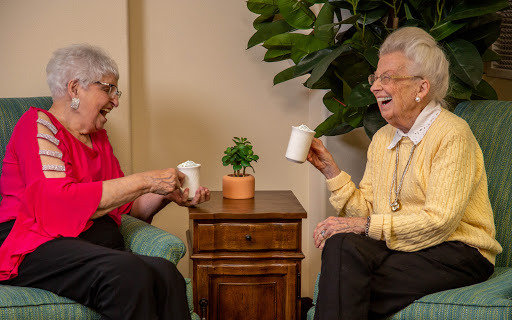 Two elderly women enjoying a joyful moment over drinks, sharing laughter in a cozy indoor setting.
