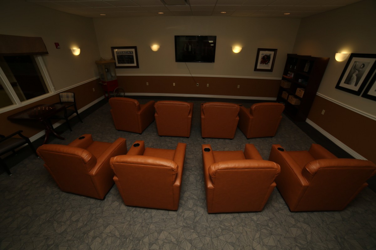 A cozy home theater setup with rows of leather chairs facing a large screen.
