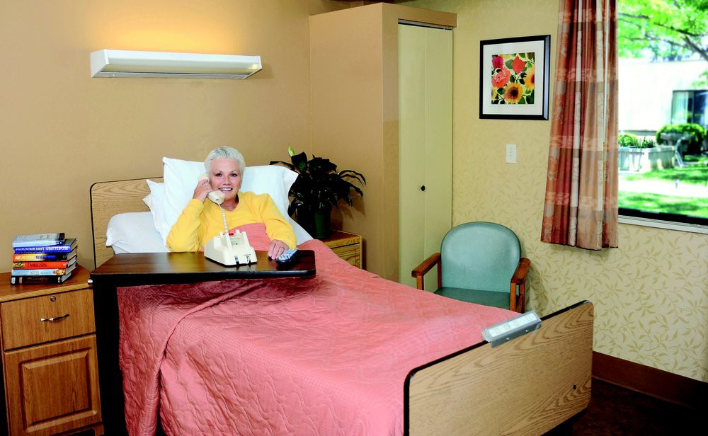An elderly person resting in a hospital bed within a warmly decorated room.