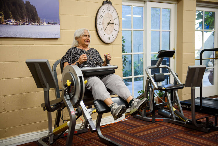 An elderly person exercising on fitness machines in a gym.