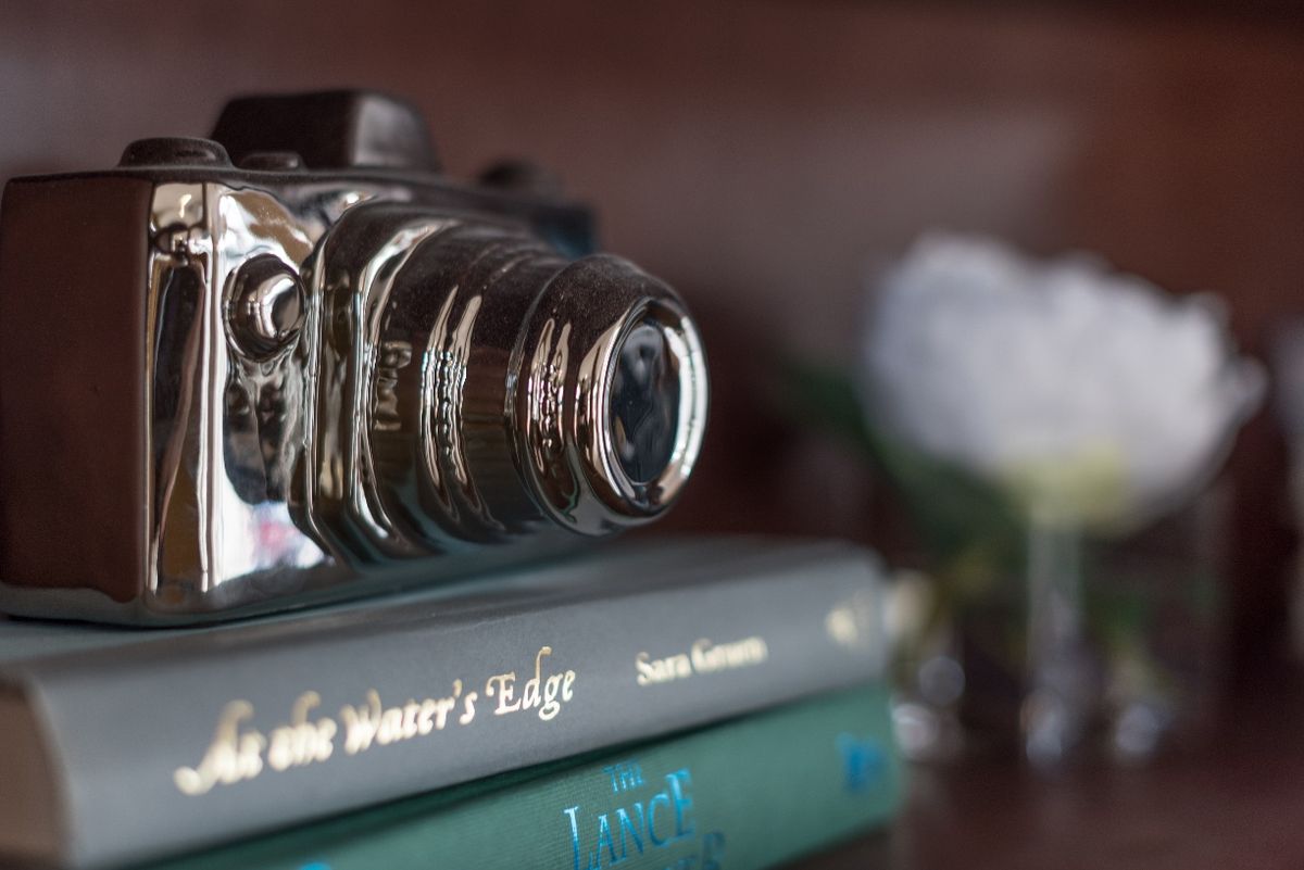 A vintage camera rests atop a stack of books on a shelf.