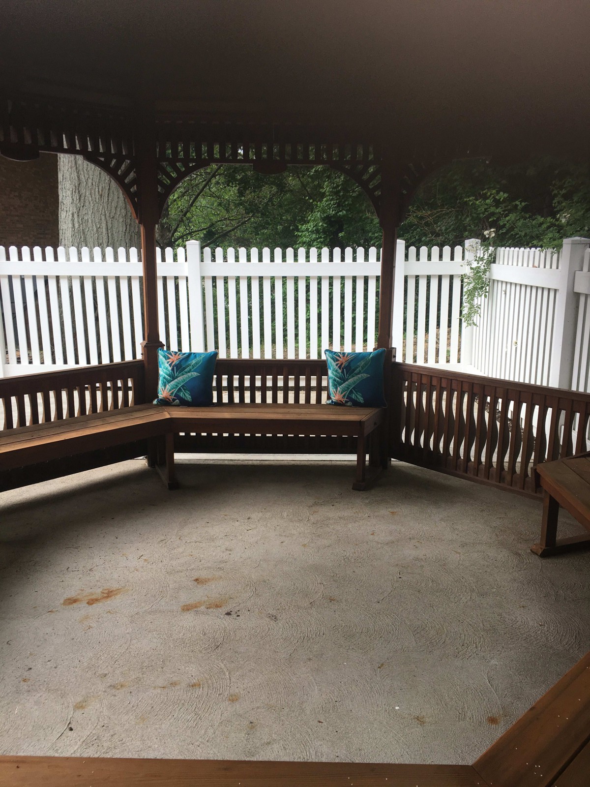 A cozy gazebo with wooden benches and blue cushions, surrounded by a white fence.