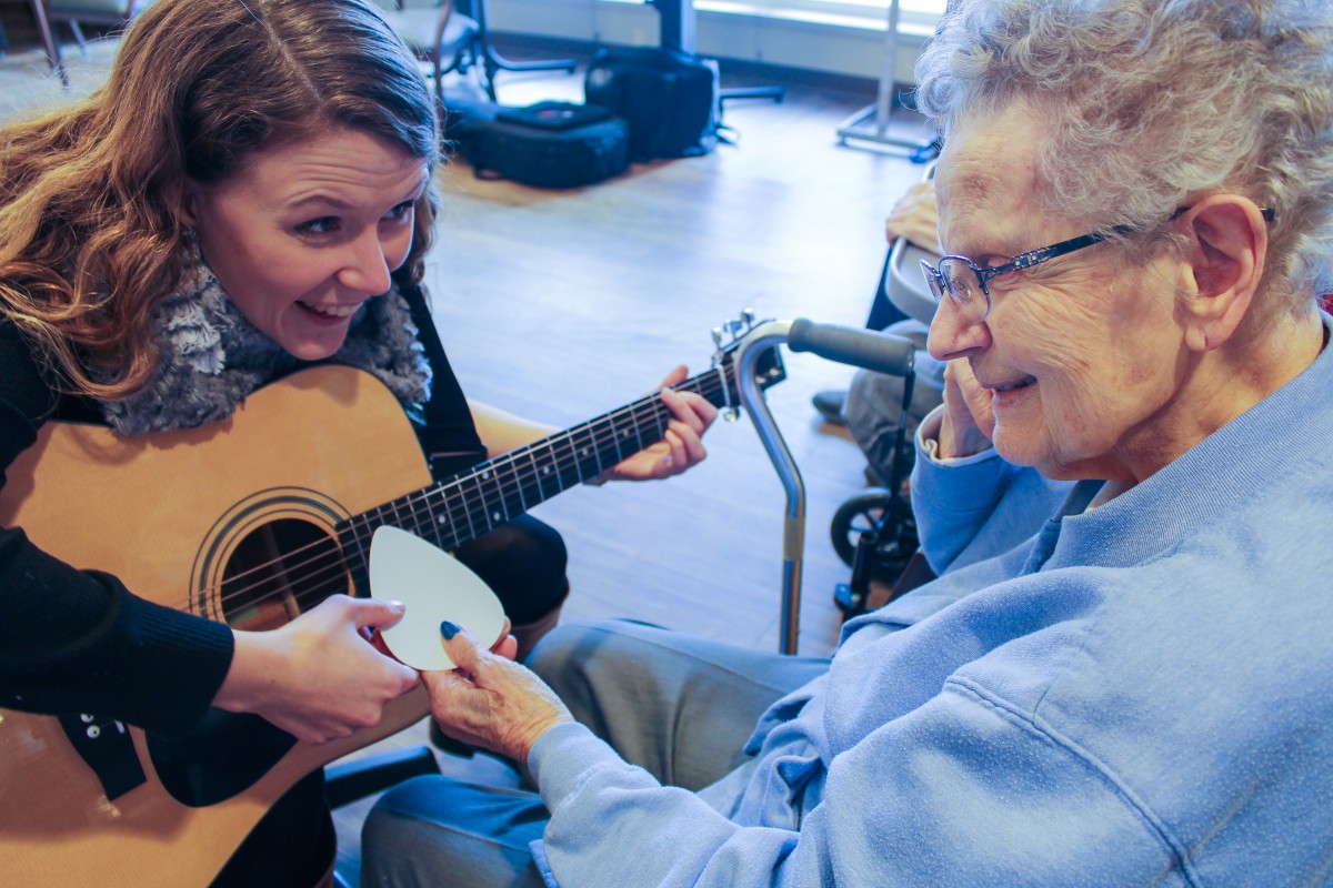 A woman plays guitar for an elderly person, sharing a moment of joy and connection through music.