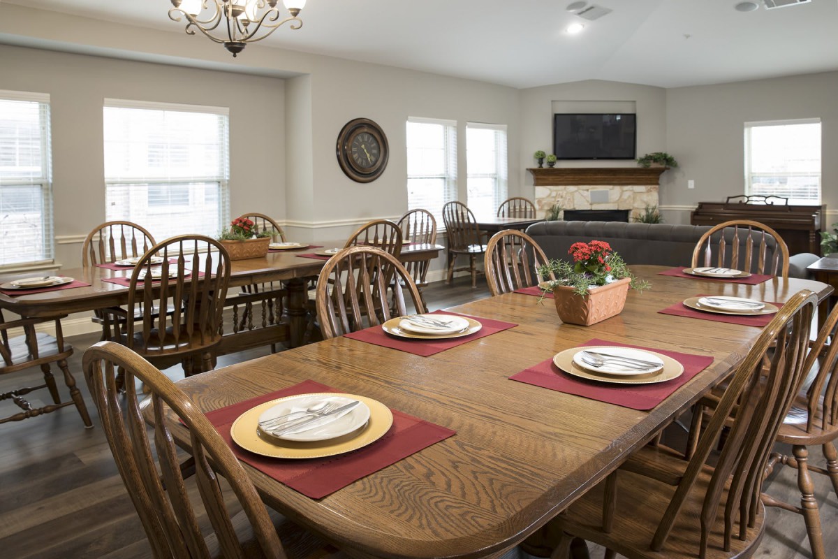 A cozy dining room with a large wooden table set for a meal, surrounded by chairs and decorated with potted plants.