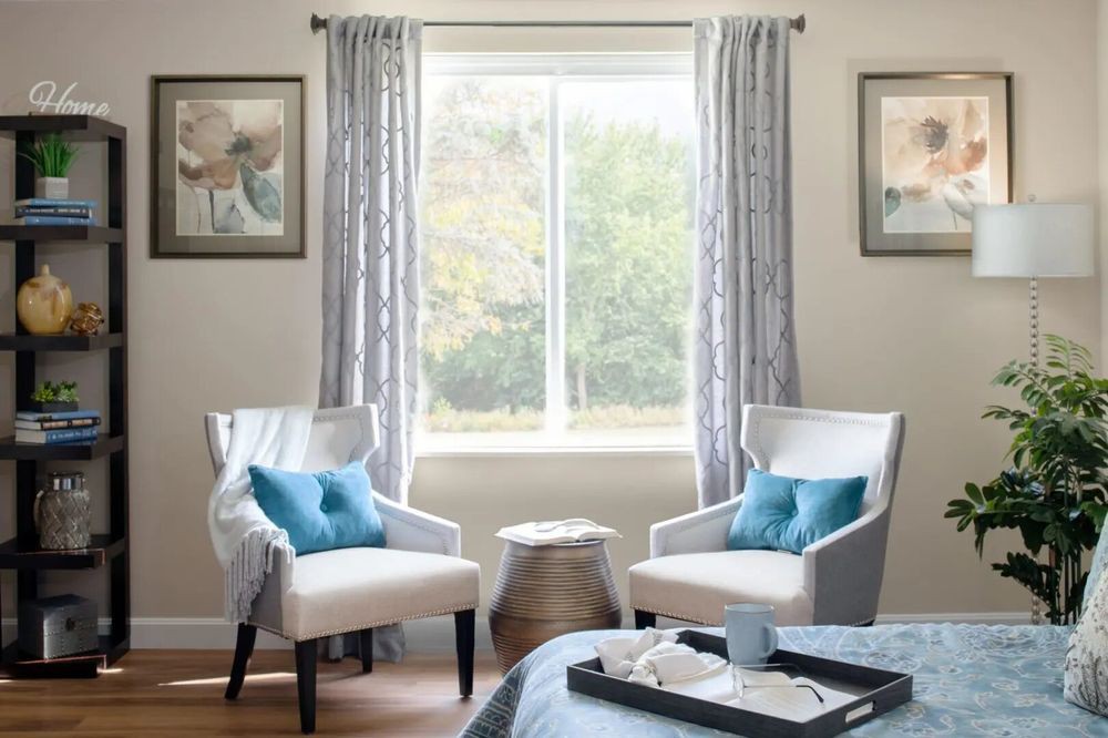 A cozy living room corner with two chairs, blue pillows, and a window view.