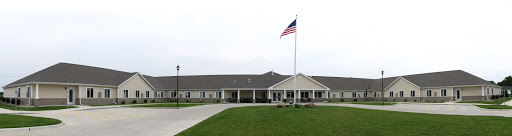 A modern facility with an American flag in front, set against a grassy landscape.