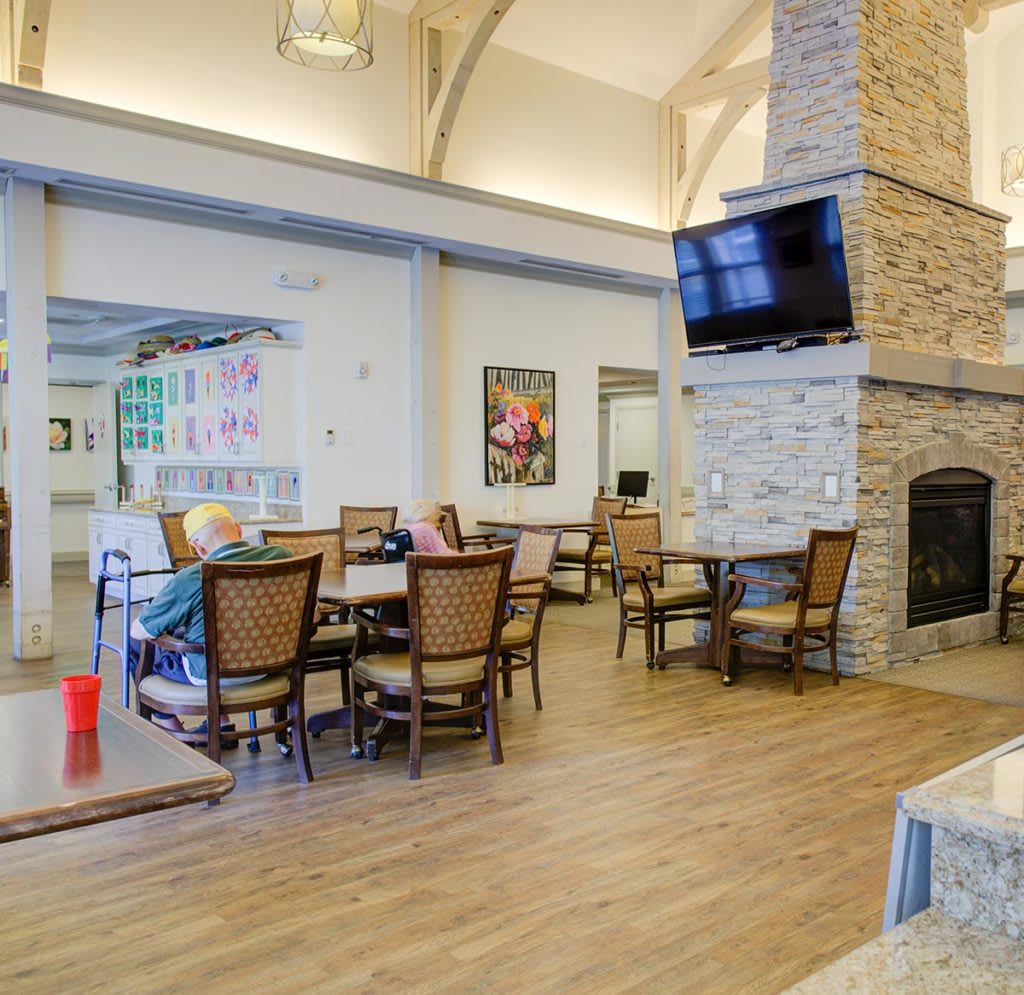 A cozy living and dining area featuring a stone fireplace, a mounted television, and wooden chairs around tables.