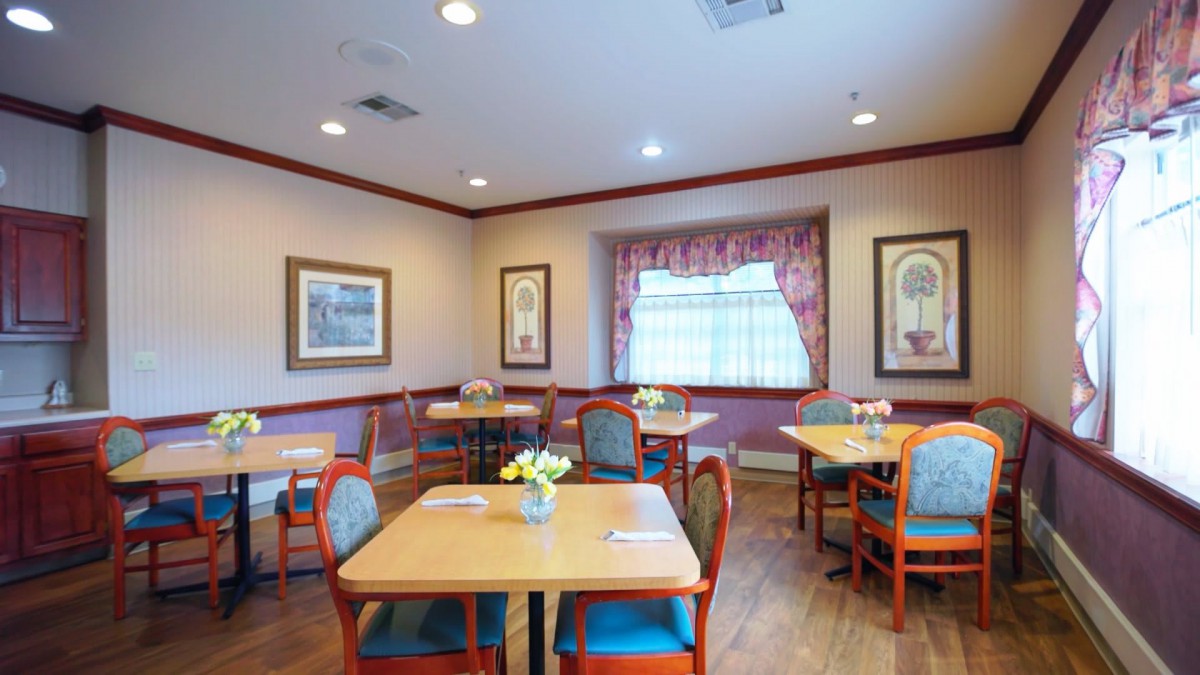 A cozy dining room with neatly arranged tables and chairs, adorned with artwork and a window with curtains.