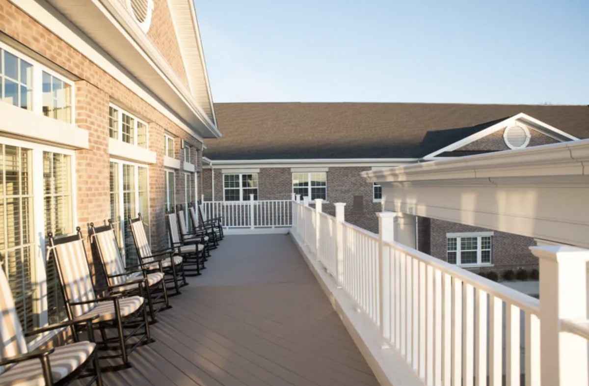 A spacious outdoor deck with white railings and several rocking chairs, attached to a residential building.