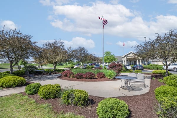 A scenic park area with well-maintained landscaping, benches, and a flagpole on a sunny day.
