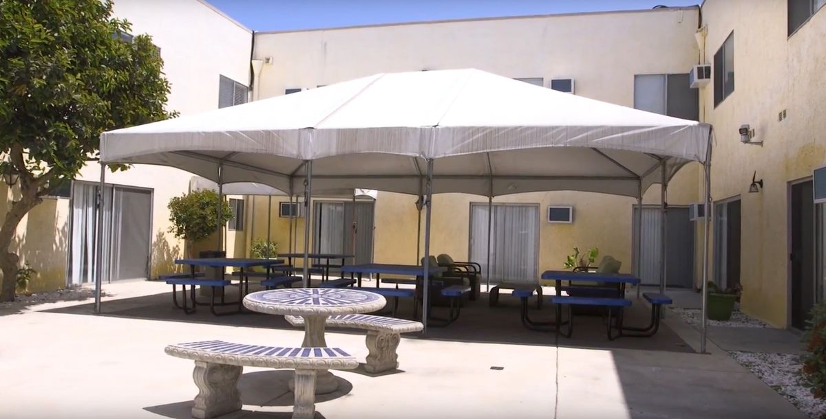 A patio area with tables and benches under a large canopy, adjacent to a building.