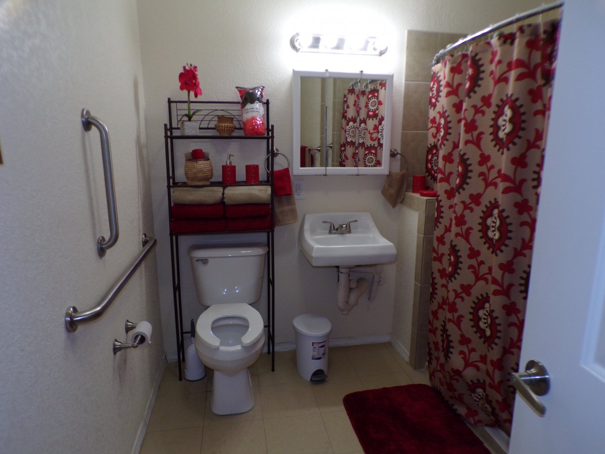 A neatly organized bathroom with a red and white color theme, featuring a toilet, sink, mirror, and shower curtain.