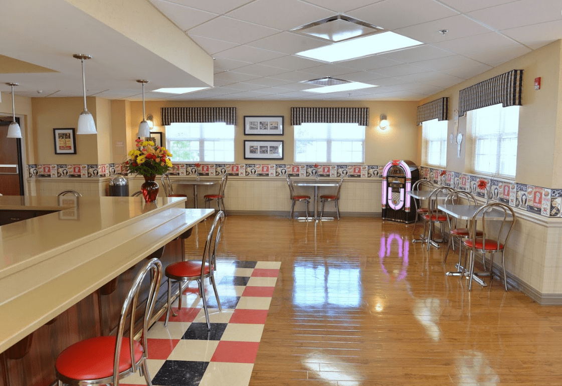 A retro-style diner with a classic jukebox, checkerboard floor, and red bar stools.