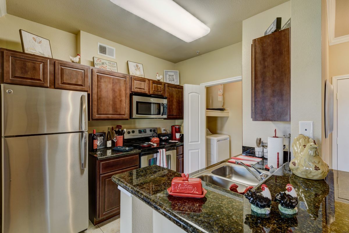 A modern kitchen in an apartment featuring stainless steel appliances, wood cabinets, and granite countertops.