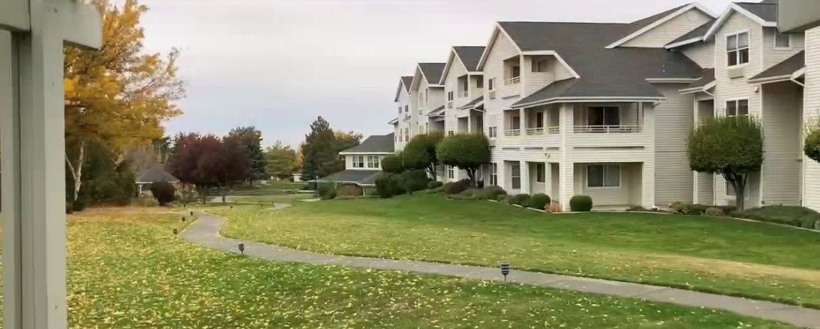 A row of suburban residential buildings with well-maintained lawns and trees on an overcast day.