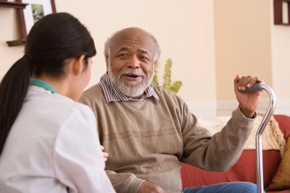 An elderly man engaged in conversation with a woman indoors.