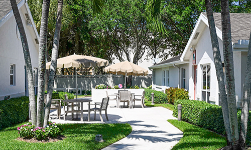 A serene garden patio with tables, chairs, and umbrellas surrounded by lush greenery.