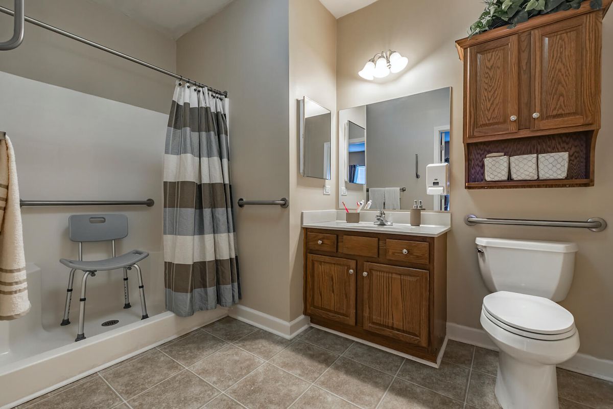 A spacious bathroom with a shower, wooden cabinet, large mirror, and modern fixtures.