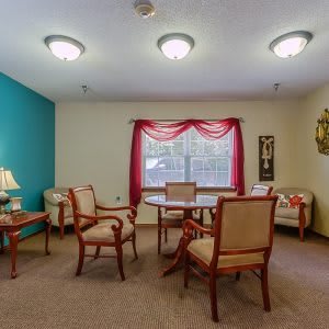 A cozy living room with a table and chairs, decorated with artwork and a lamp.
