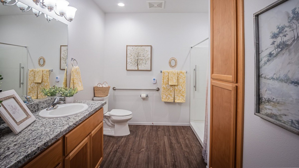 A modern bathroom with a sleek shower, toilet, and sink area, featuring hardwood floors and neatly arranged towels.