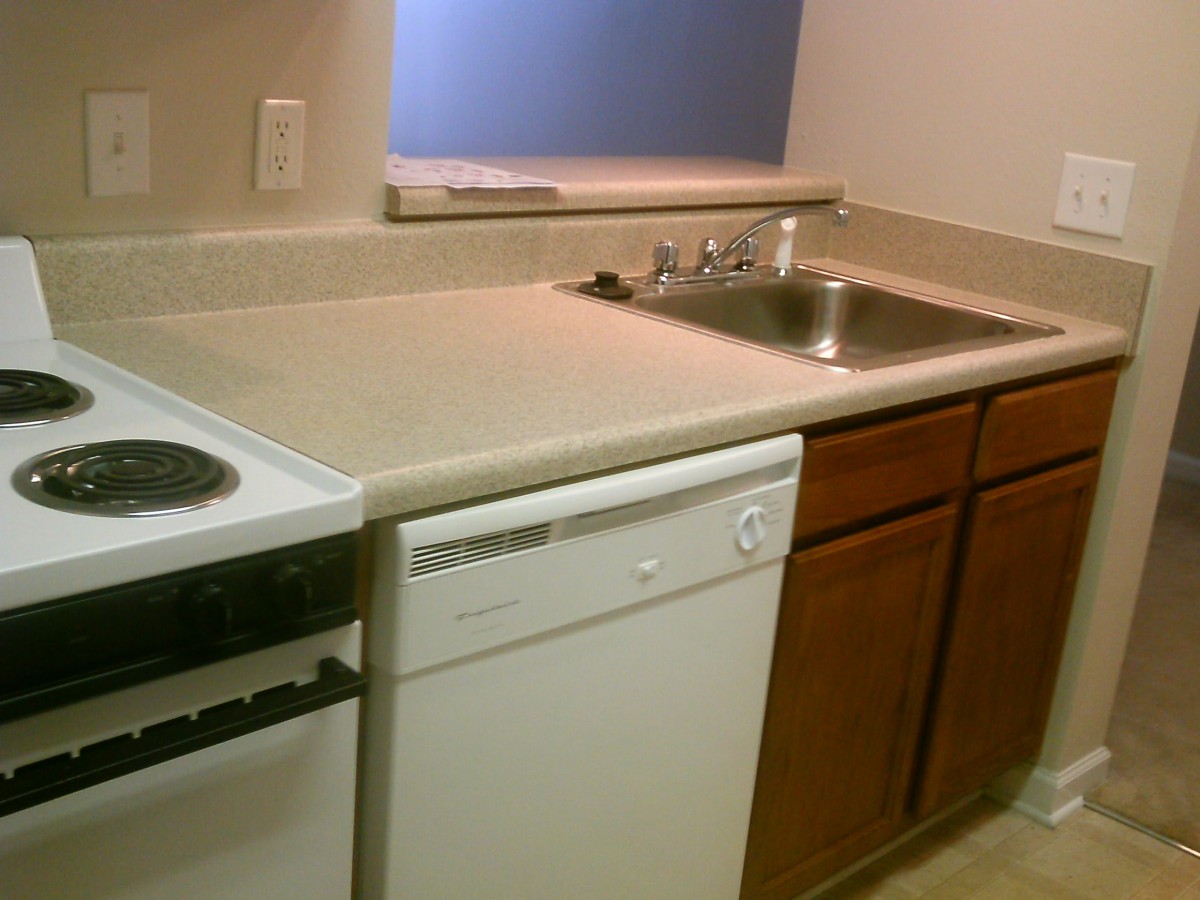 A compact kitchen area featuring a sink and dishwasher with wooden cabinets.