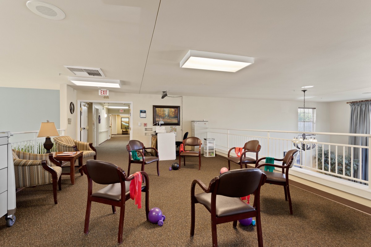 A community room with chairs arranged for activities, featuring a carpeted floor and recreational items.