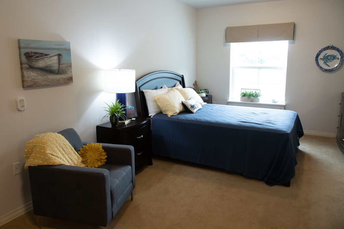 A neatly arranged bedroom with a single bed, armchair, and a lamp near the window.