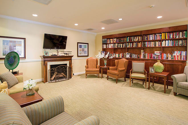 A cozy library with a seating area, featuring armchairs and a television above the fireplace.