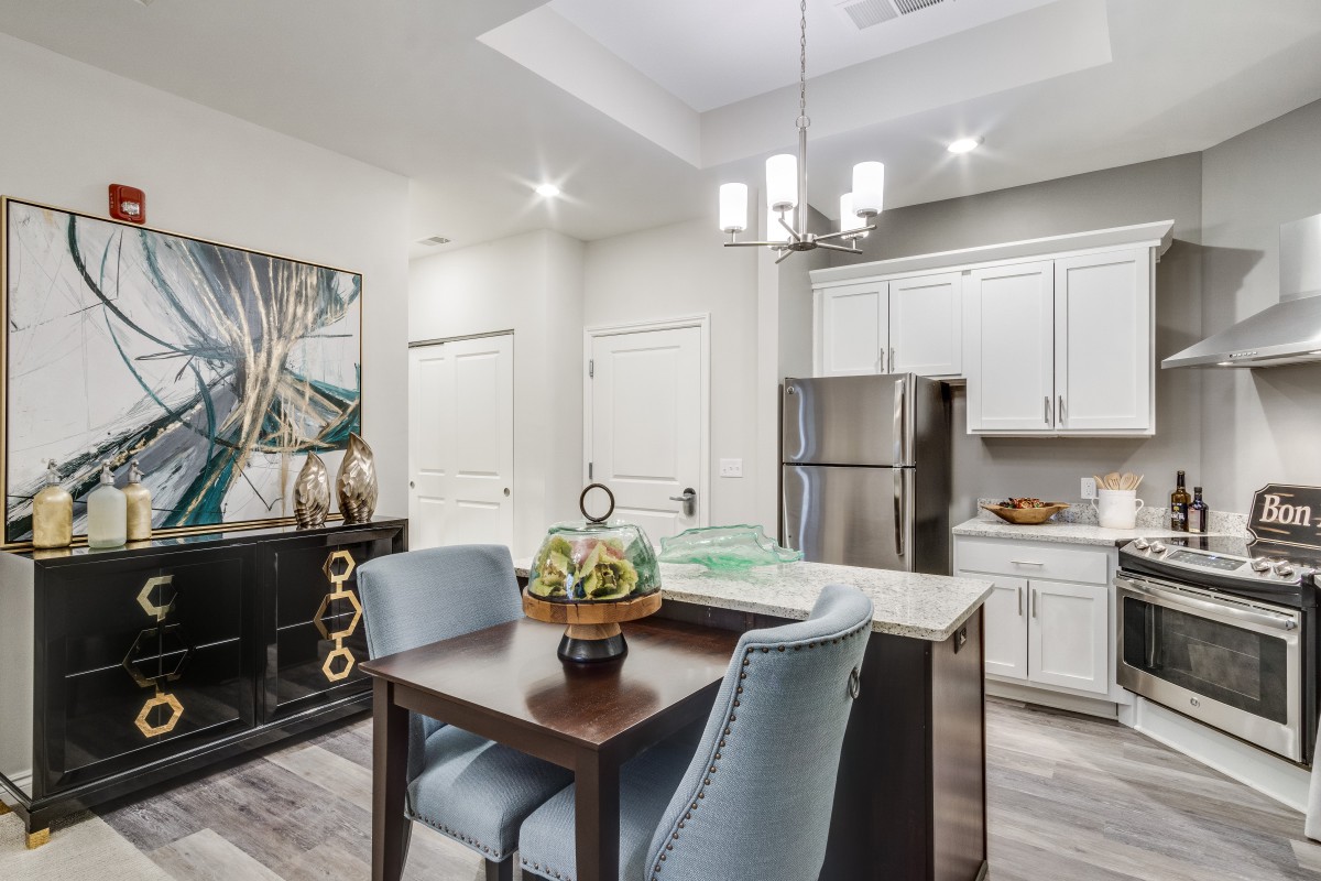 A modern kitchen and dining area featuring stainless steel appliances, white cabinetry, and elegant artwork.