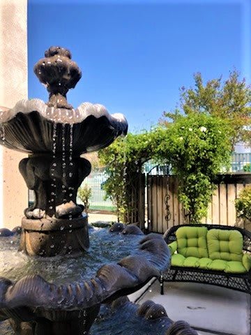 A tranquil garden patio featuring a beautiful stone fountain and cozy green cushioned seating.