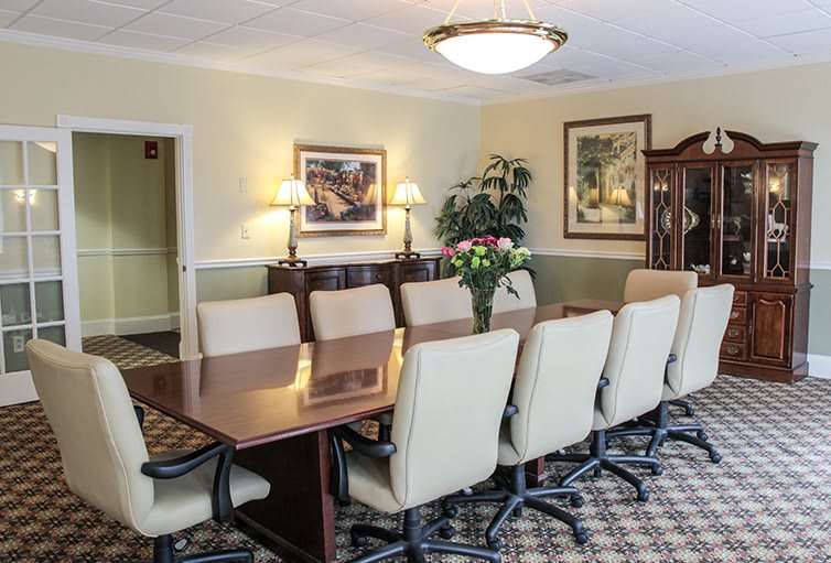 A well-furnished conference room with a long table and office chairs surrounded by wall decor and plants.