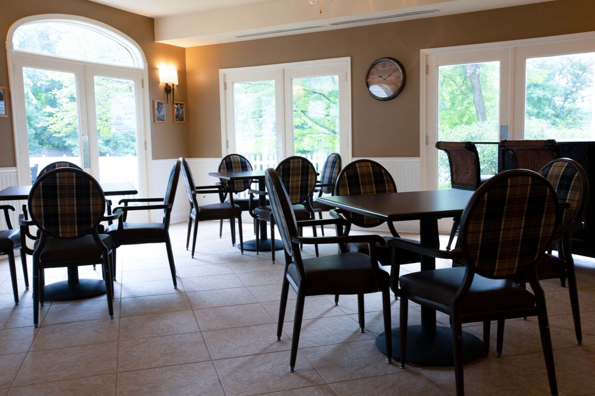 An empty dining area with several tables and chairs, illuminated by natural daylight from large windows.