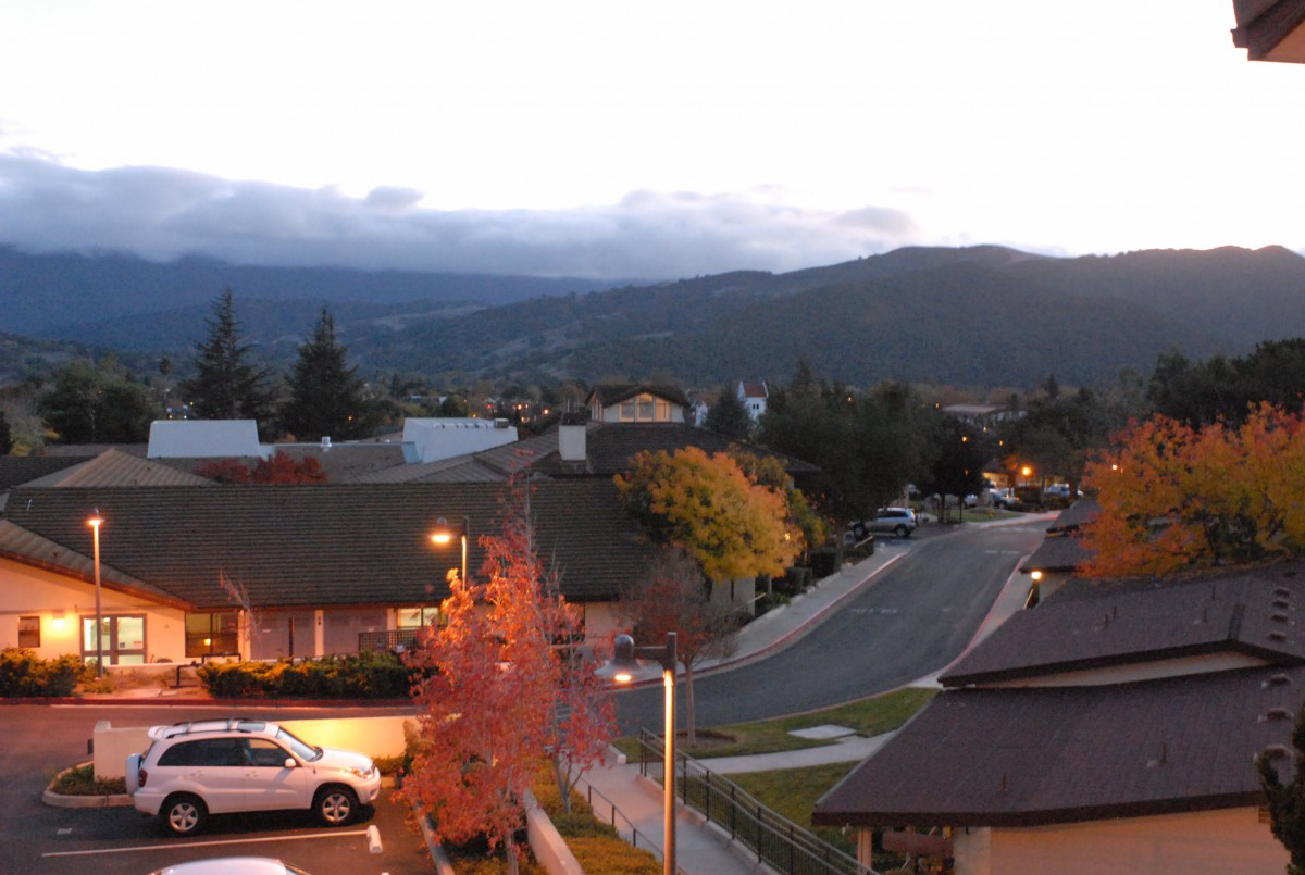 A peaceful suburban neighborhood at dusk with houses lining the street and mountain views in the background.