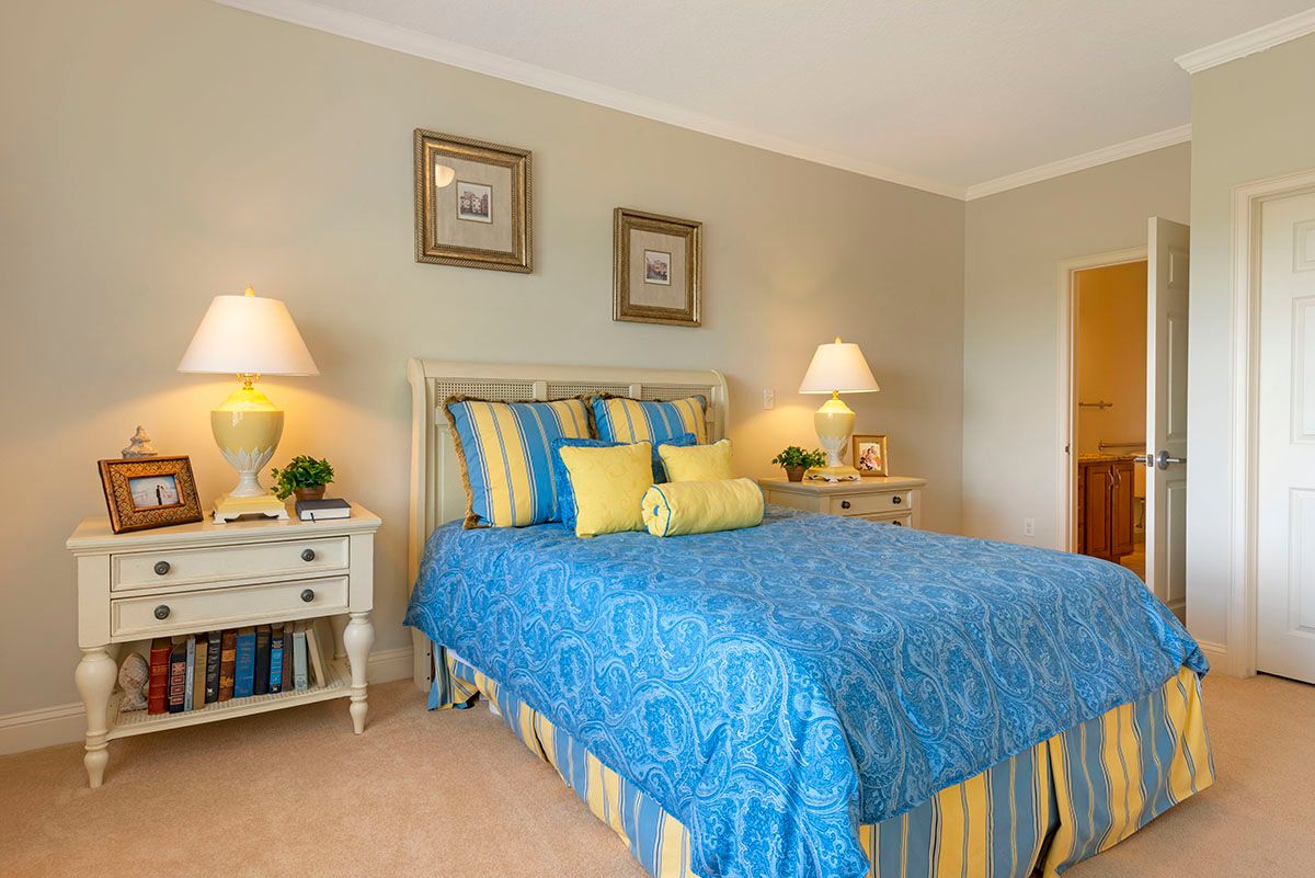A cozy bedroom featuring a bed with blue patterned bedding and striped pillows, flanked by two nightstands with lamps. Framed artwork adorns the walls.