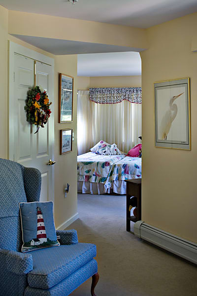 A cozy interior view looking towards a bedroom through a hallway, featuring a decorated wreath on the door and colorful bedspread.