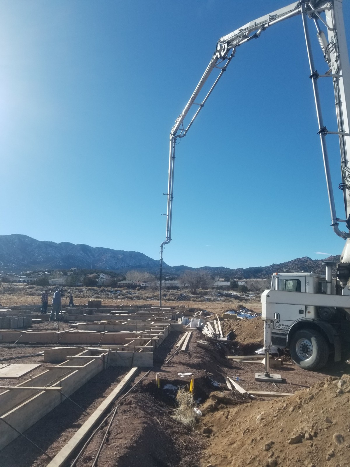 A construction site with a cement pump truck operating under a clear blue sky, set against a backdrop of mountains.