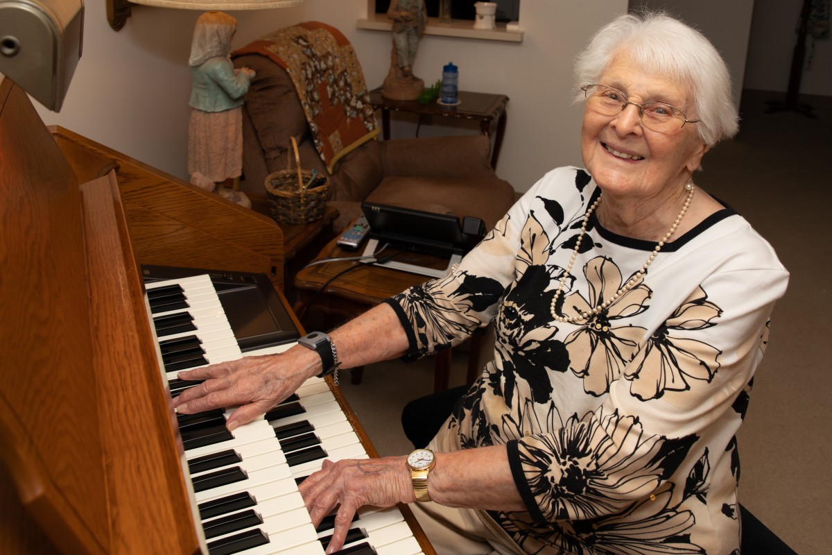 An elderly woman happily playing the piano in a cozy home setting.